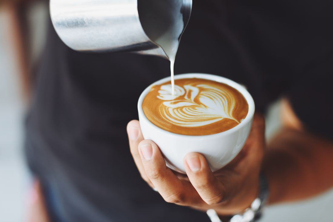 Barista menuang susu membuat latte art di cangkir kopi